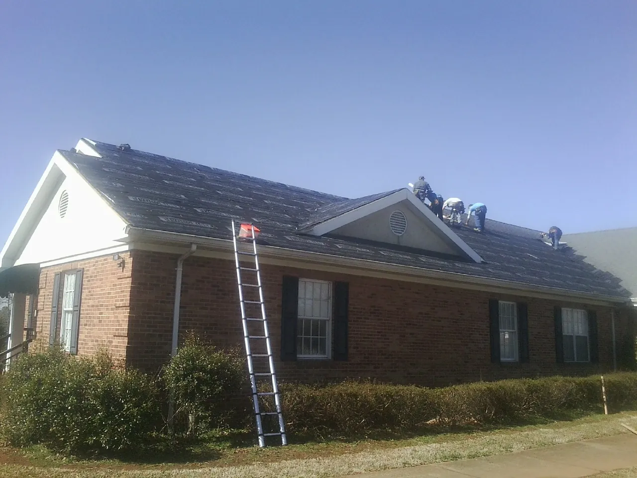 Crew tearing shingles off a brick ranch roof with a ladder set — Metal Roof Repair work by our crew in Fiskeville