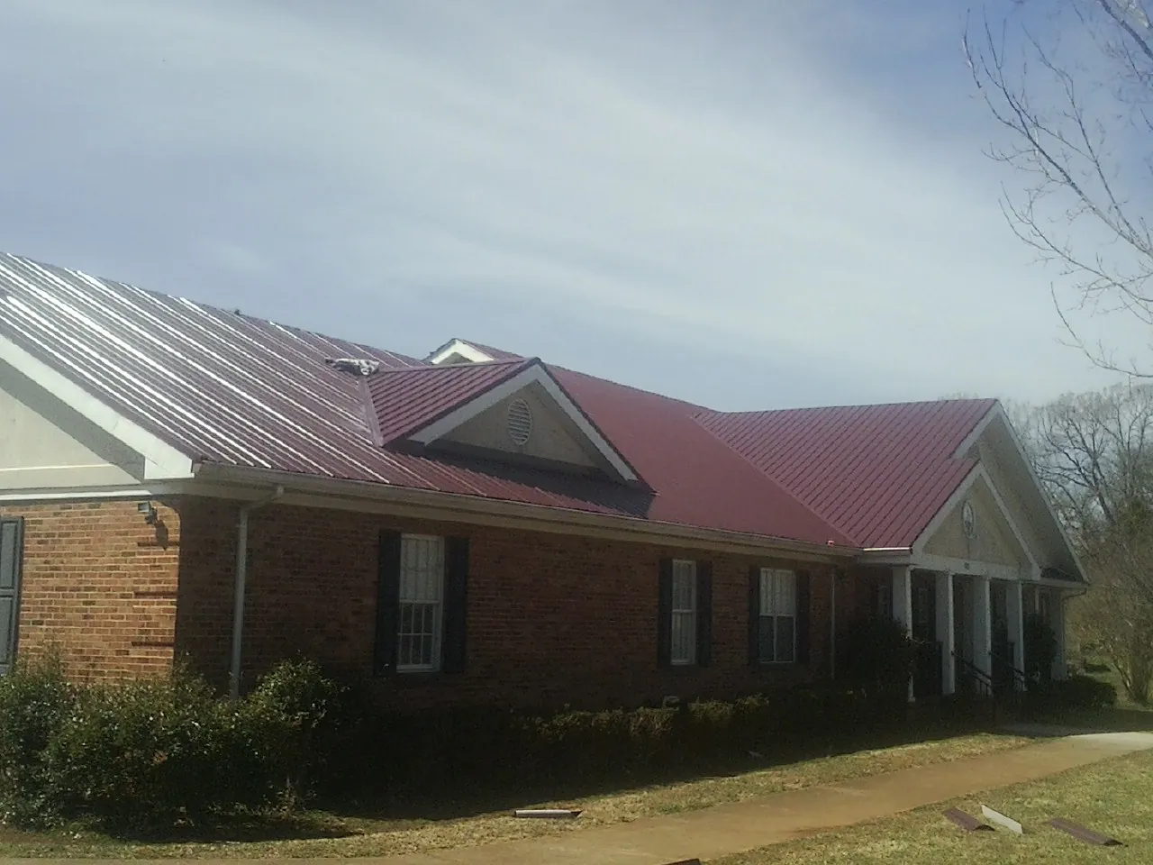 Red metal roof with gabled entries on a long brick building, from a Hail Damage Roof Repair job in Fiskeville