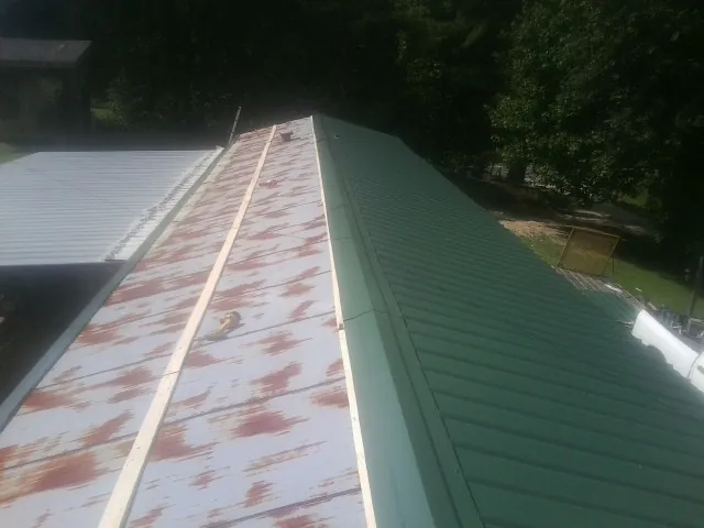 Old rusted panels beside newly installed green metal roofing — Wind Damage Roof Repair by Roofing Brothers in Fiskeville