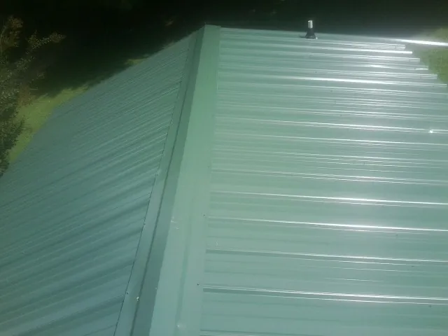 New green metal panels meeting at the ridge of a roof — Flat Roof Repair work by our crew in Fiskeville