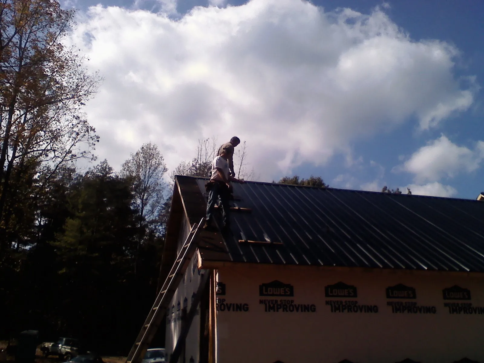 Roofer fastening dark metal panels high against a cloudy sky, from a Roof Inspection job in Fiskeville