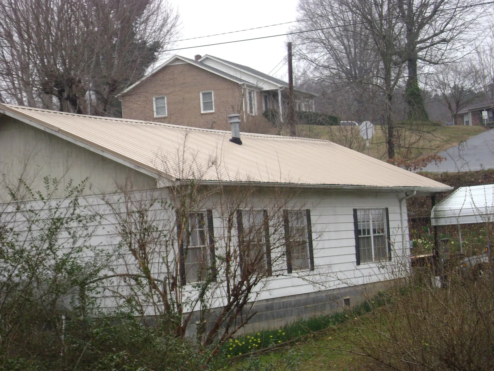 Tan metal roof on a white sided house set into a hillside — Commercial Roofing by Roofing Brothers in Fiskeville