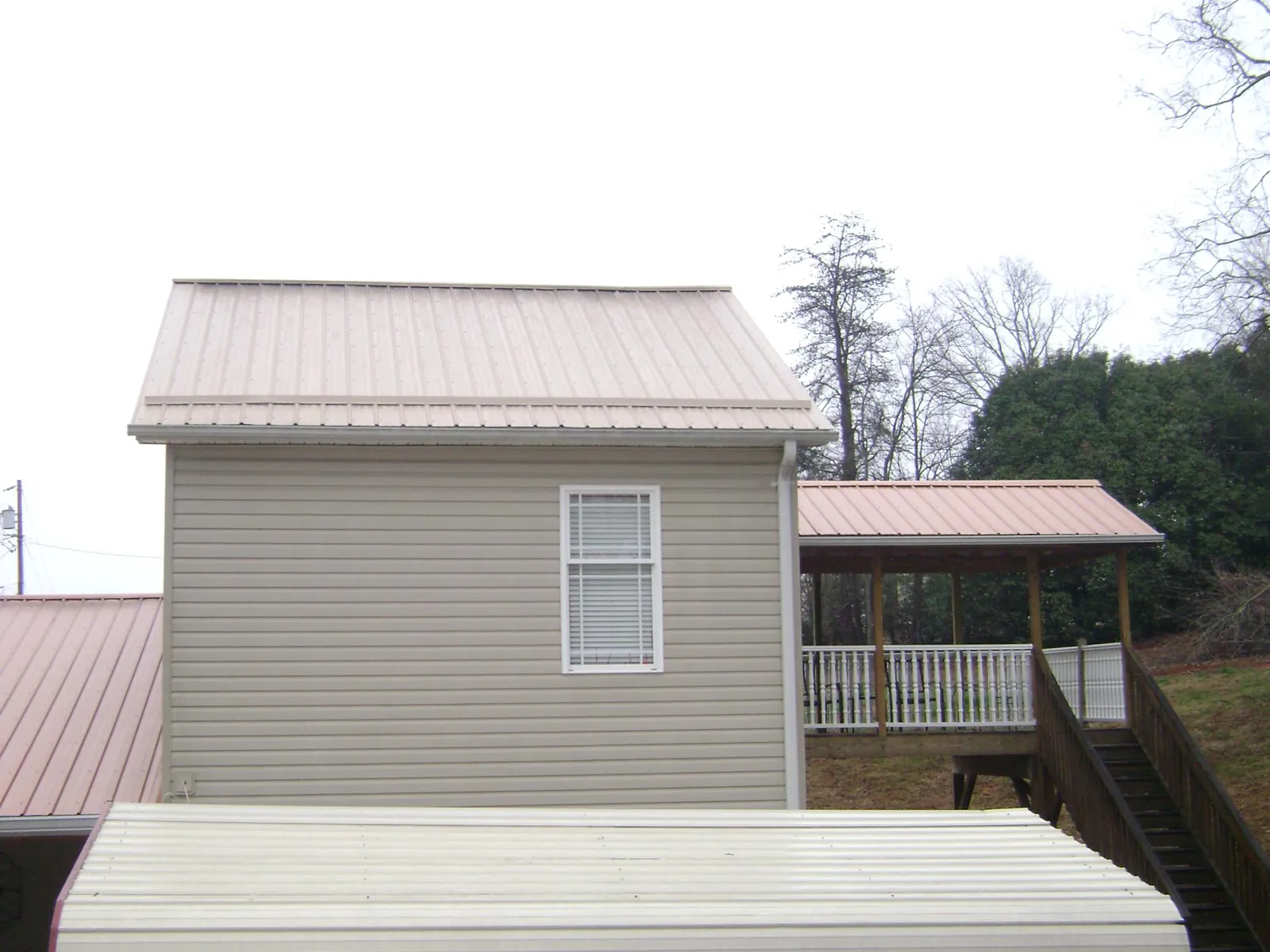 Tan metal roofs on a two story addition and attached porch, from a Roof Replacement job in Fiskeville